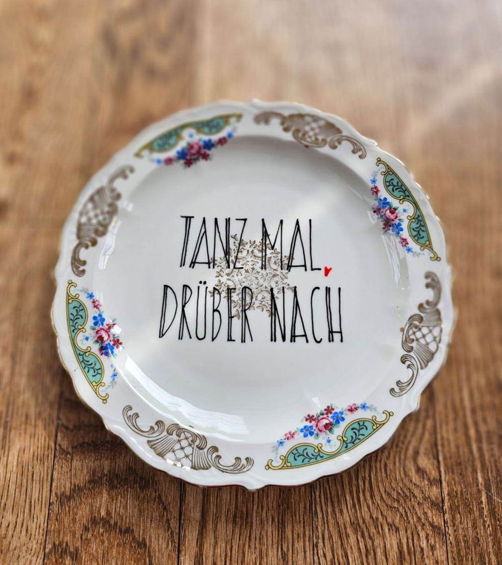 Vintage-Teller mit goldenen Verzierungen und dem handgeschriebenen Spruch 'Tanz mal drüber nach' in schwarzer Schrift.